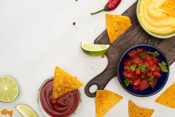 Vista superior de nachos de milho com limão, pimenta, ketchup e molho de queijo em tábua de corte de madeira sobre fundo branco — Fotografia de Stock