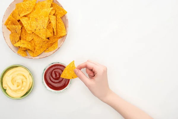 Cropped view of woman eating corn nachos with cheese sauce and ketchup on white background — Stock Photo