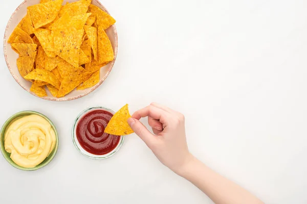 Vista recortada de la mujer comiendo nachos de maíz con salsa de queso y ketchup sobre fondo blanco - foto de stock