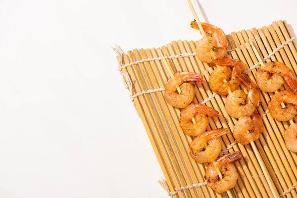 Top view of prawns on skewers on bamboo mat on white background — Stock Photo