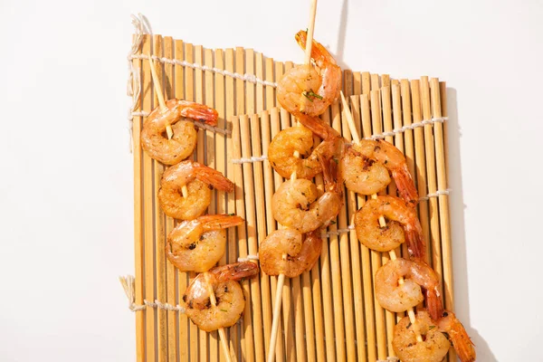 Vista superior de langostinos en brochetas sobre estera de bambú sobre fondo blanco — Stock Photo