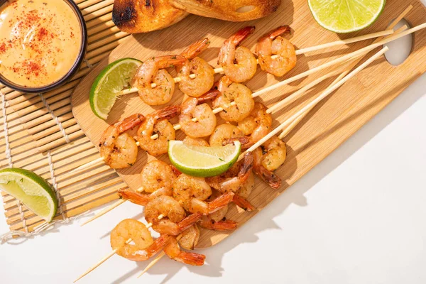 Top view of prawns on skewers with lime and sauce on bamboo mat on white background — Stock Photo