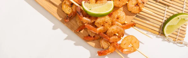 Top view of prawns on skewers with lime on bamboo mat on white background, panoramic orientation — Stock Photo