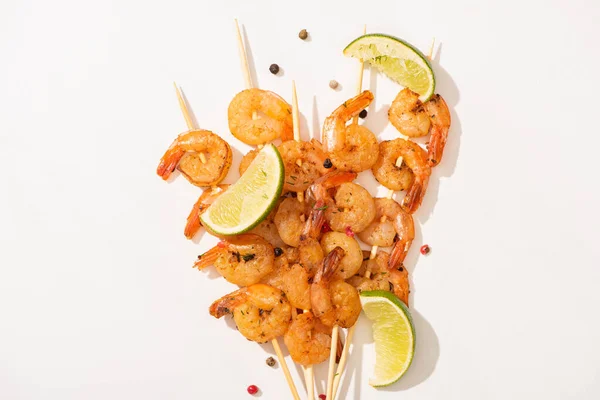 Vue de dessus des crevettes sur brochettes avec citron vert et poivre noir sur fond blanc — Photo de stock