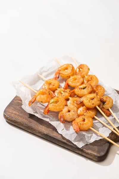 Prawns on skewers on parchment paper on wooden board on white background — Stock Photo