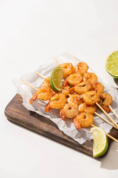 Crevettes sur brochettes à la chaux sur papier parchemin sur carton de bois sur fond blanc — Photo de stock