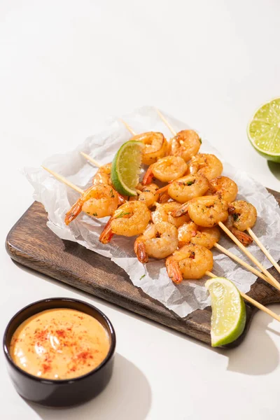 Prawns on skewers with lime and sauce on parchment paper on wooden board on white background — Stock Photo