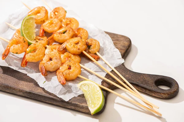 Prawns on skewers with lime on parchment paper on wooden board on white background — Stock Photo