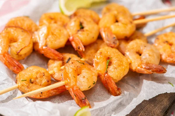 Close up view of prawns on skewers with lime on parchment paper on wooden board — Stock Photo