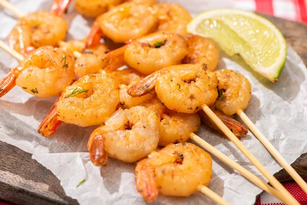 Vista de cerca de las gambas en brochetas con cal sobre papel pergamino sobre tabla de madera - foto de stock