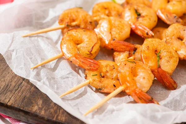 Close up view of prawns on skewers on parchment paper on wooden board — Stock Photo