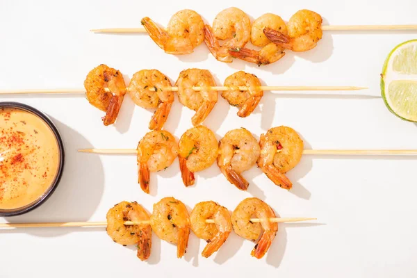 Top view of delicious fried prawns on skewers with lime and sauce on white background — Stock Photo