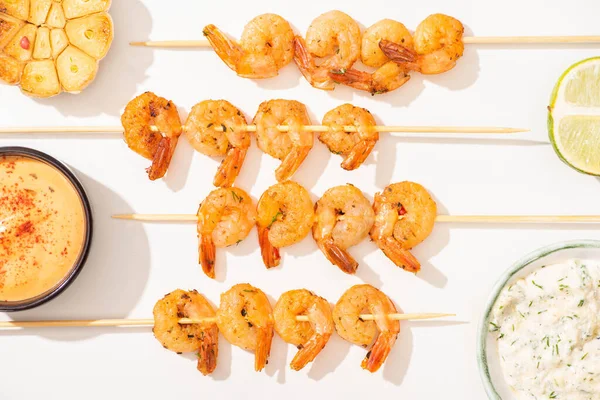 Vue de dessus de délicieuses crevettes frites sur brochettes avec ail, citron vert et sauces sur fond blanc — Photo de stock