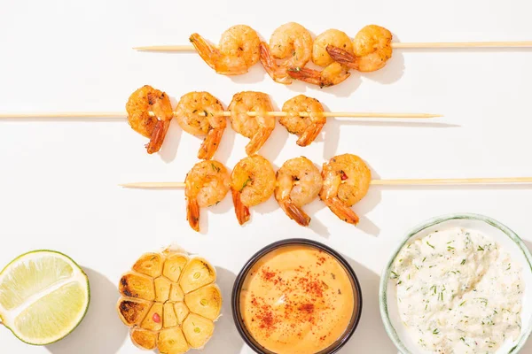 Vue de dessus de délicieuses crevettes frites sur brochettes avec ail, citron vert et sauces sur fond blanc — Photo de stock