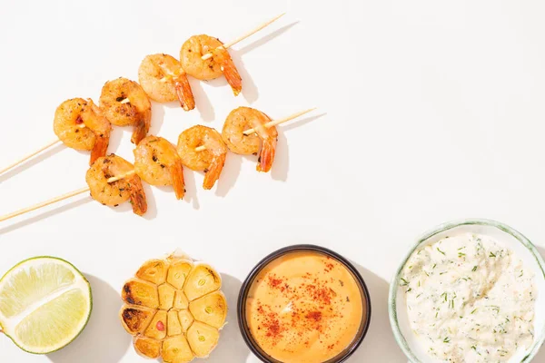 Vista superior de deliciosos langostinos fritos en pinchos con ajo, lima y salsas sobre fondo blanco - foto de stock