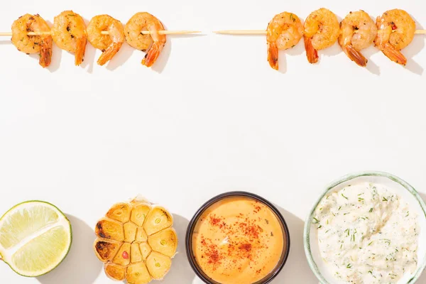 Vista superior de deliciosos langostinos fritos en pinchos con ajo, lima y salsas sobre fondo blanco - foto de stock