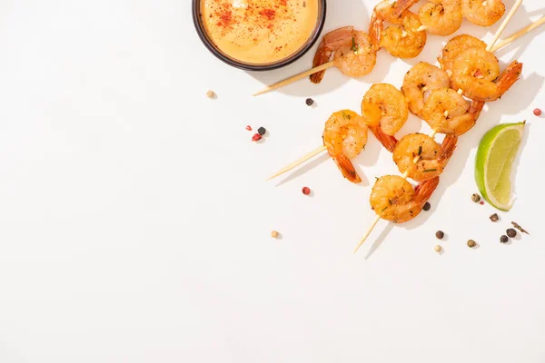 Vista superior de deliciosos langostinos fritos en pinchos con salsa, lima y pimienta sobre fondo blanco - foto de stock