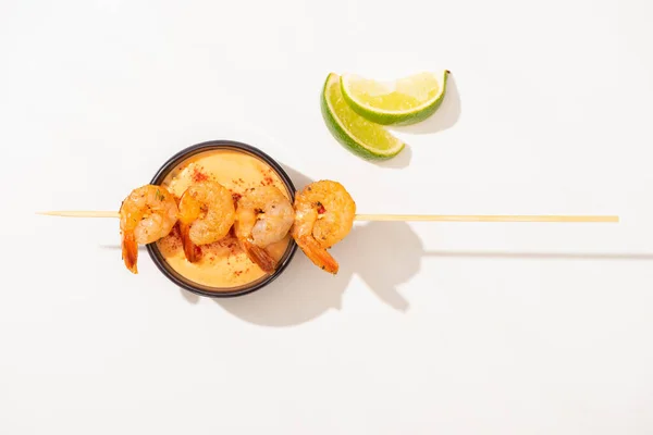 Vue de dessus de délicieuses crevettes frites sur brochette avec citron vert et sauce sur fond blanc — Photo de stock