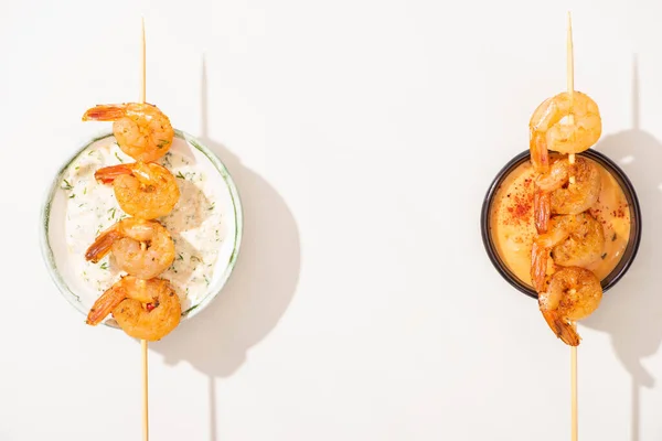 Vista superior de deliciosos langostinos fritos en pinchos con salsas sobre fondo blanco - foto de stock