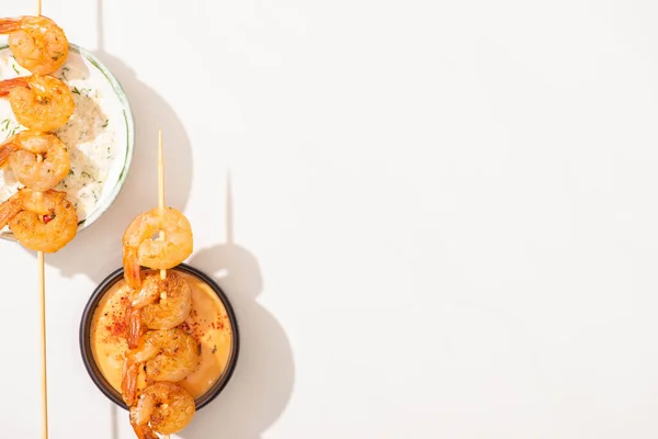 Вид вкусных жареных креветок на шампуры с соусами на белом фоне — стоковое фото
