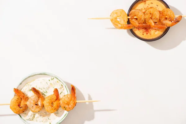 Vue de dessus de délicieuses crevettes frites sur brochettes avec des sauces sur fond blanc — Photo de stock