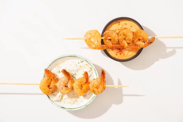 Vue de dessus de délicieuses crevettes frites sur brochettes avec des sauces sur fond blanc — Photo de stock