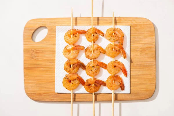 Top view of fried prawns on skewers on wooden board on white background — Stock Photo