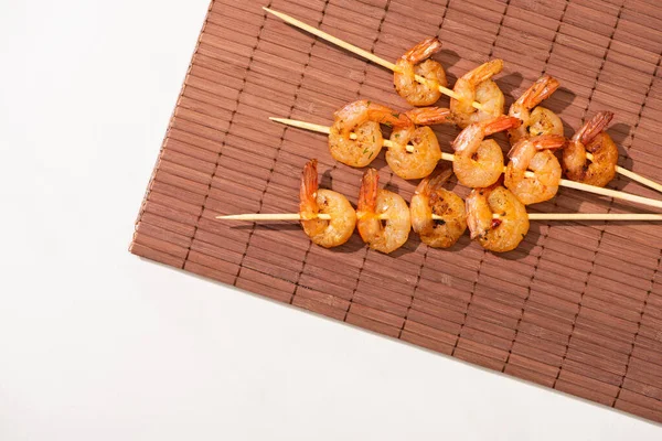 Top view of fried prawns on skewers on bamboo mat on white background — Stock Photo