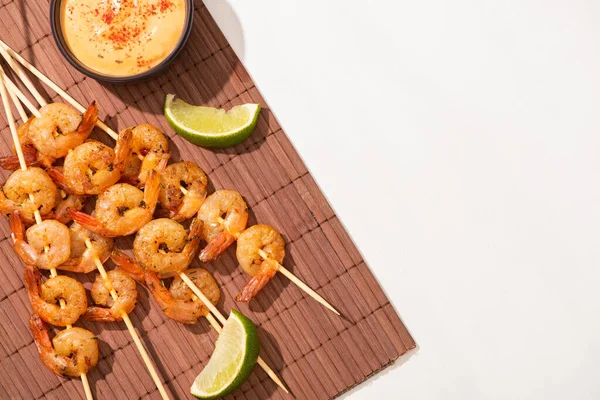 Vue du dessus des crevettes sur brochettes à la lime et sauce sur tapis de bambou sur fond blanc — Photo de stock