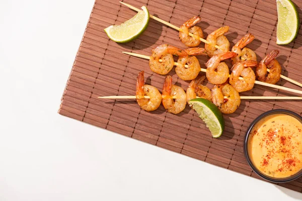 Vue du dessus des crevettes sur brochettes à la lime et sauce sur tapis de bambou sur fond blanc — Photo de stock