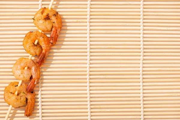 Vista superior de sabrosos langostinos en brochetas en estera de bambú beige — Stock Photo