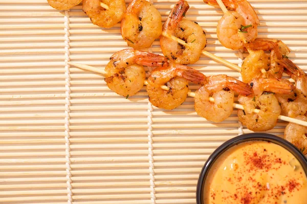 Vista superior de sabrosos langostinos en pinchos con salsa en estera de bambú beige - foto de stock