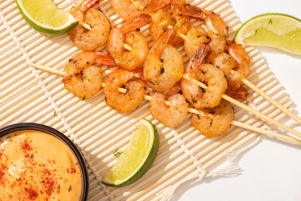 Top view of prawns on skewers with lime and sauce on bamboo mat on white background — Stock Photo