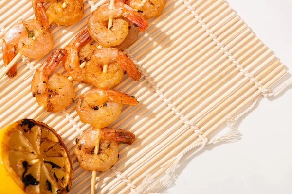 Top view of prawns on skewers with grilled lemon on bamboo mat on white background — Stock Photo