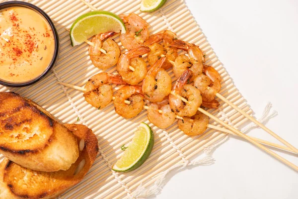 Draufsicht auf Garnelen am Spieß mit gegrilltem Brot, Limette und Soße auf Bambusmatte auf weißem Hintergrund — Stockfoto