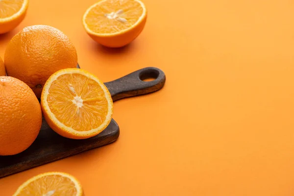 Ripe delicious cut and whole oranges on wooden cutting board on colorful background — Stock Photo