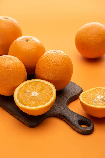 Mûr juteux ensemble et couper des oranges sur planche à découper en bois sur fond coloré — Photo de stock