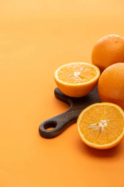 Mûr juteux ensemble et couper des oranges sur planche à découper en bois sur fond coloré — Photo de stock