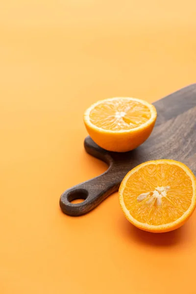 Mitades anaranjadas jugosas maduras sobre tabla de cortar de madera sobre fondo colorido - foto de stock