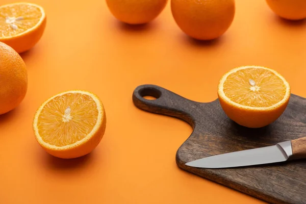 Frische saftige ganze und geschnittene Orangen auf Schneidebrett mit Messer auf buntem Hintergrund — Stockfoto