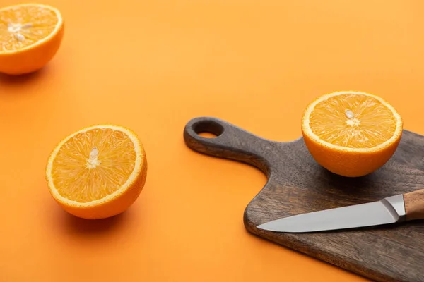 Fresh juicy cut oranges on cutting board with knife on colorful background — Stock Photo