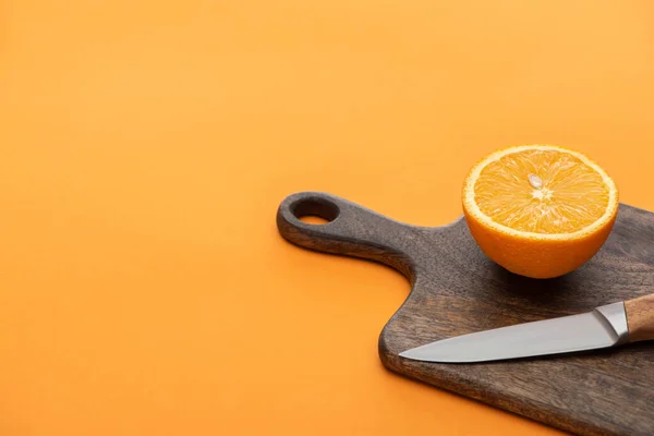 Fresh juicy orange half on cutting board with knife on colorful background — Stock Photo