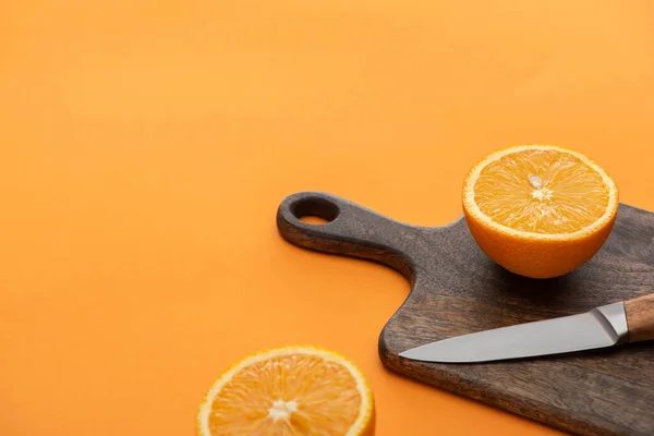 Fresh juicy orange halves on cutting board with knife on colorful background — Stock Photo