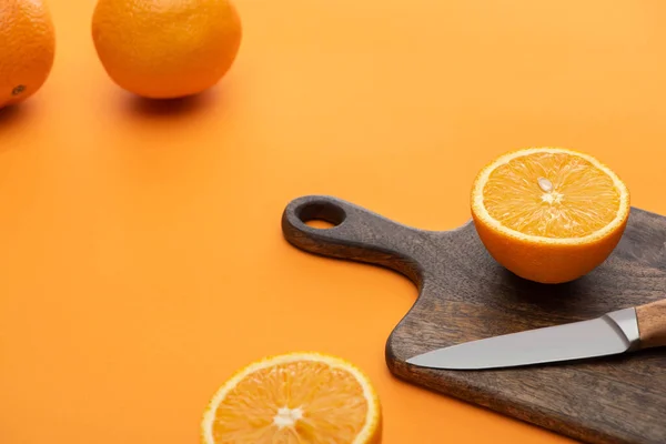 Fresche succose arance intere e tagliate sul tagliere con coltello su sfondo colorato — Foto stock