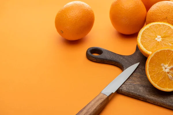 Fresh juicy whole and cut oranges on cutting board with knife on colorful background — Stock Photo