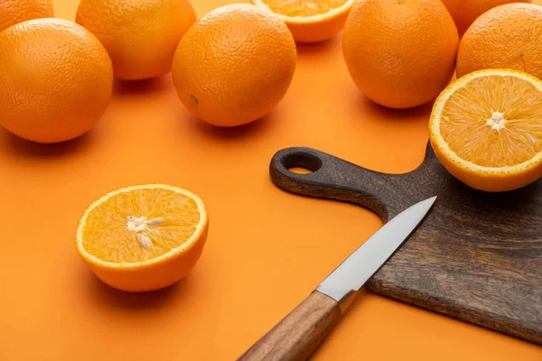 Frische saftige ganze und geschnittene Orangen auf Schneidebrett mit Messer auf buntem Hintergrund — Stockfoto