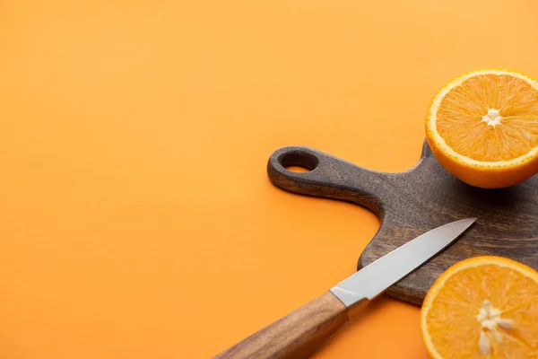 Mitades de naranja jugosas frescas en la tabla de cortar con cuchillo sobre fondo colorido - foto de stock