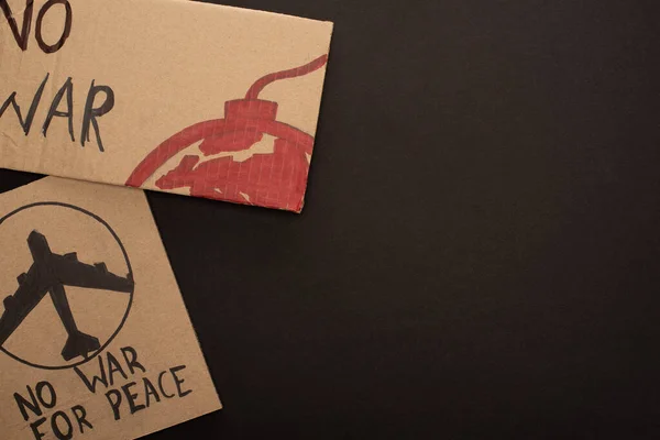 Top view of cardboard placards with no war lettering, plane and bomb on black background — Stock Photo