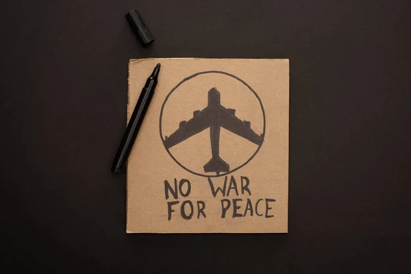 Зверху вид на картонний плакат без війни за мирний напис і літак біля позначки на чорному тлі. — стокове фото