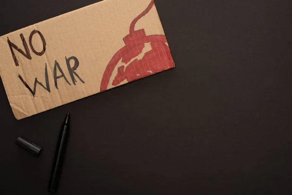 Top view of marker and cardboard placard with no war lettering and bomb on black background — Stock Photo